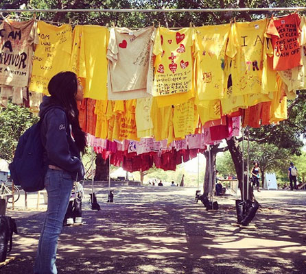 student looking at messages from sexual assault survivors written on t-shirts hanging on a clothesline